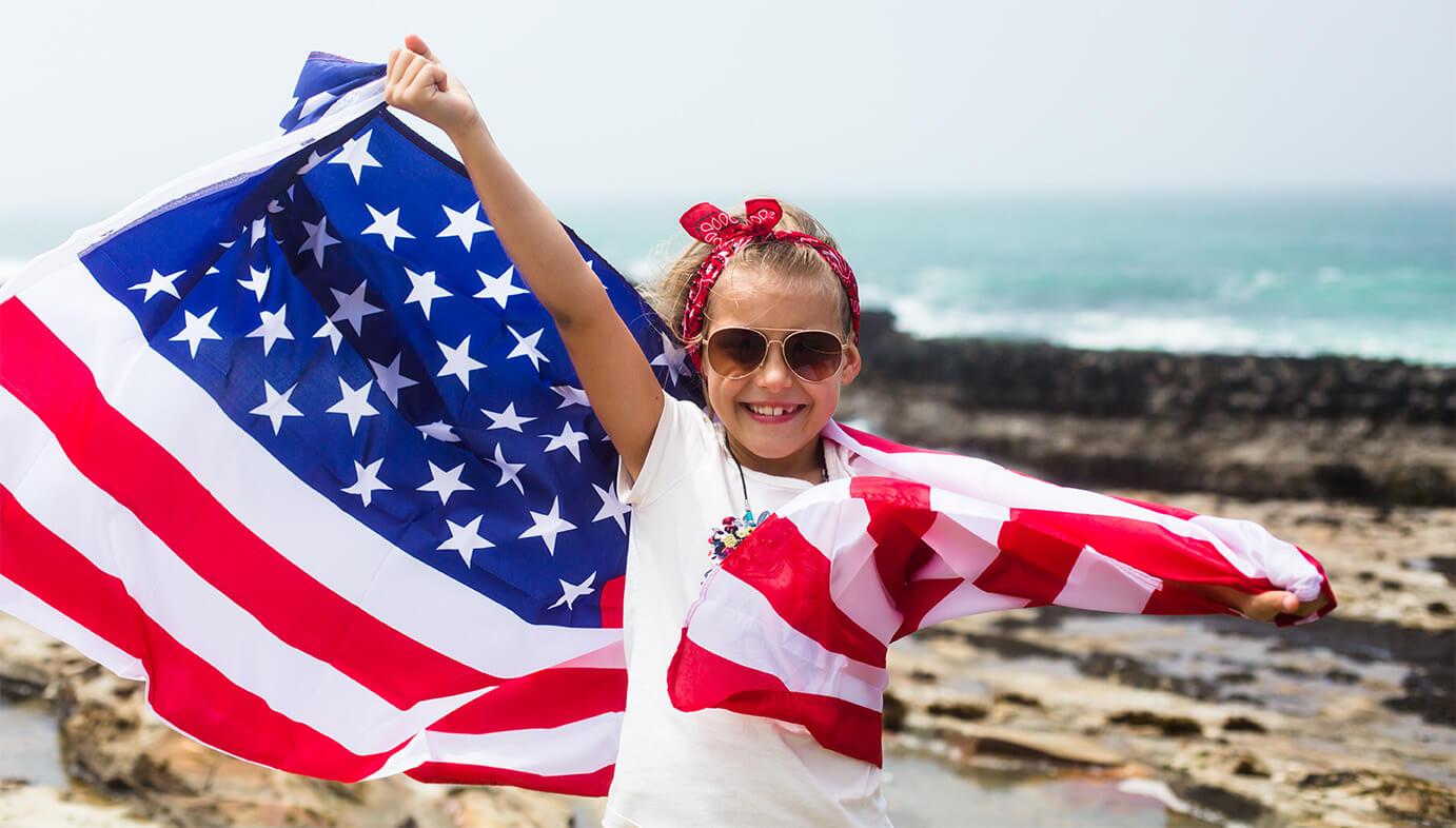 A girl holding an American flag on a beach